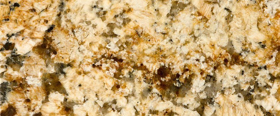 A close-up view of granite stone with a speckled, textured pattern of cream, tan, brown, and black minerals.