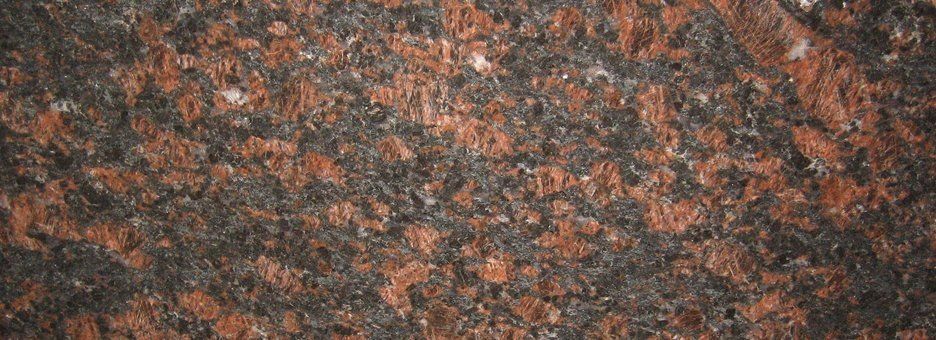 A close-up of a polished granite slab with a mottled pattern of dark charcoal, reddish-brown, and white minerals.