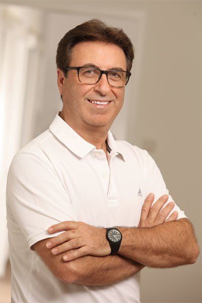 Gözlüklü, gülümseyen, kollarını kavuşturmuş, beyaz polo tişört ve saat takan adam.
