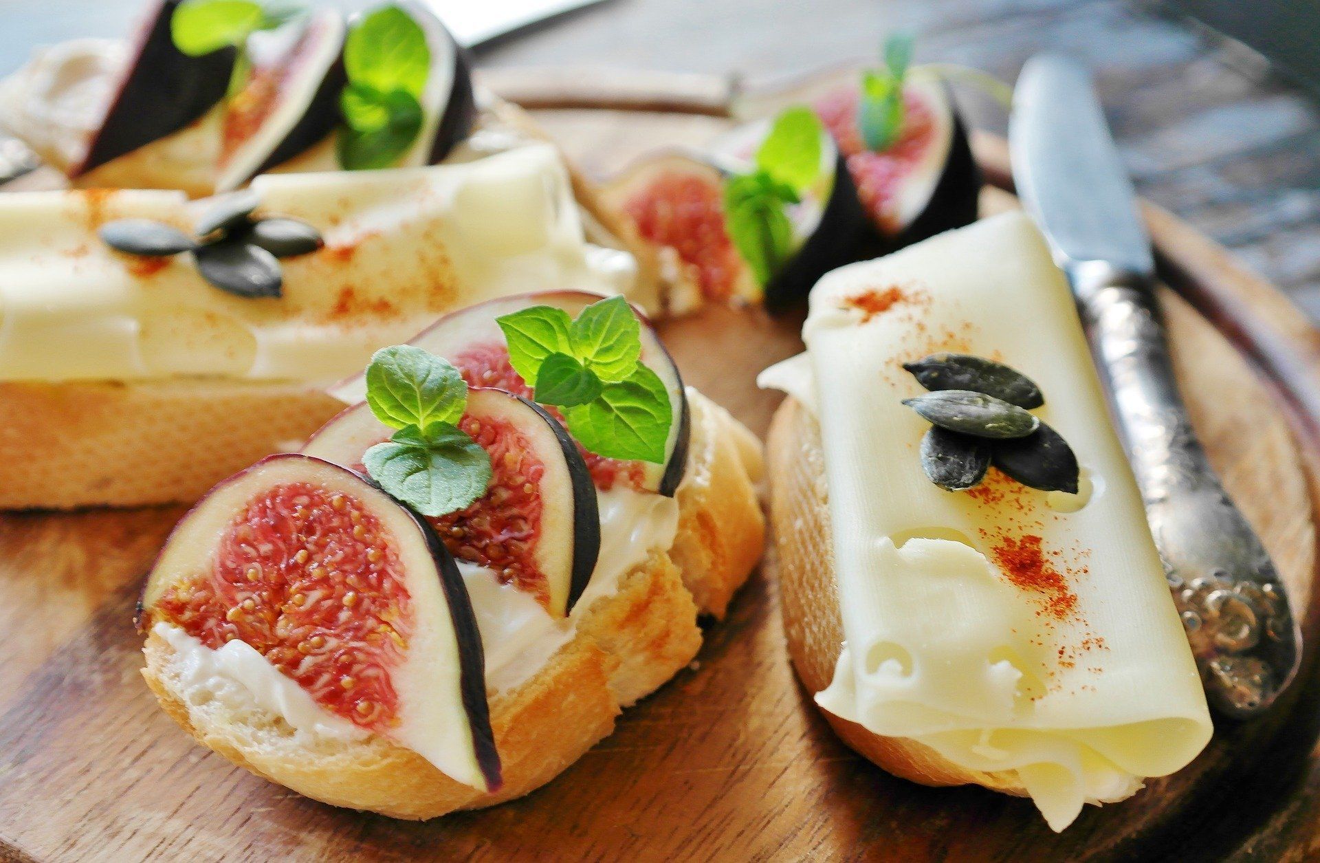 Ein hölzernes Schneidebrett, belegt mit Brot, Käse, Feigen und Minzblättern.