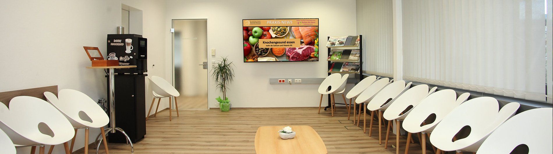 Beyaz sandalyelerin, tahta bir masanın ve yemek resimlerinin gösterildiği bir televizyonun bulunduğu bir bekleme odası.