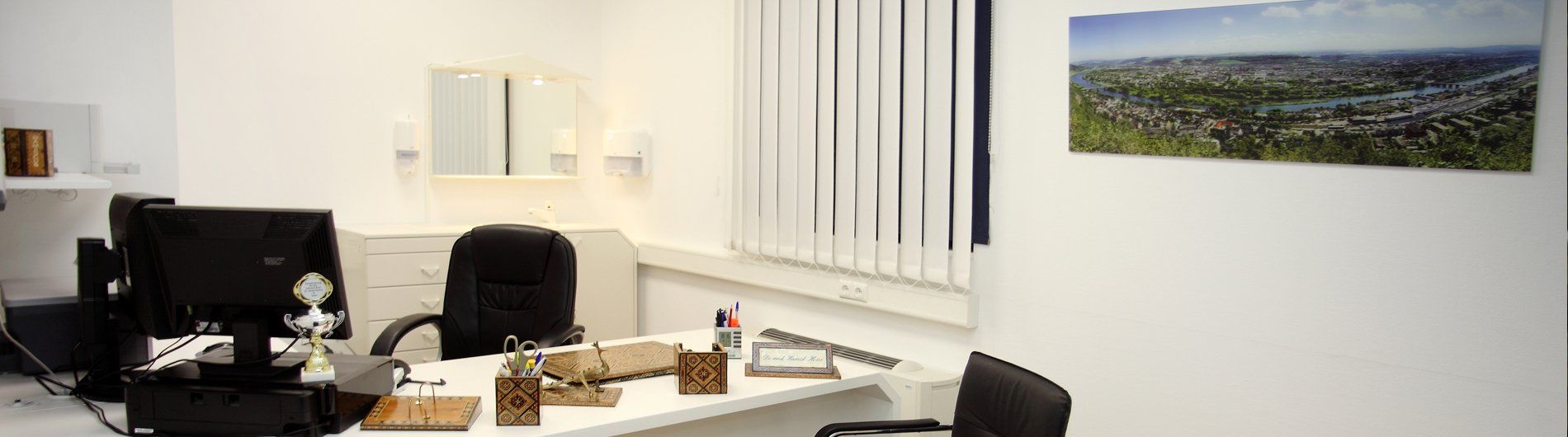 Çalışma masası, sandalye, bilgisayar, pencere panjurları ve manzara fotoğrafı bulunan ofis.