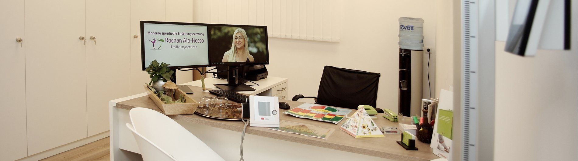 İki monitör, bir tansiyon aleti ve diğer eşyaların bulunduğu dağınık bir ofis masası.