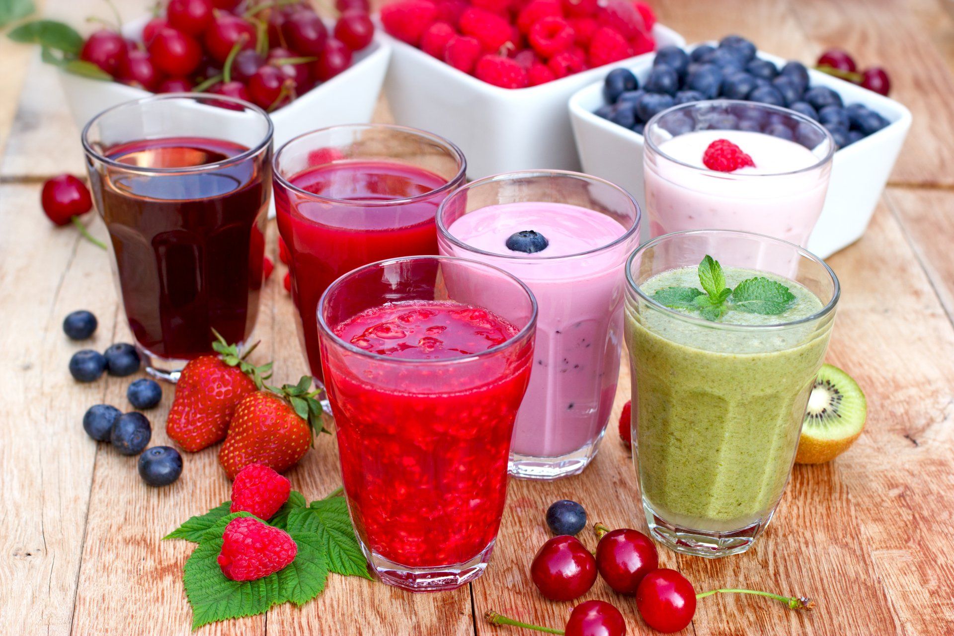 Ein Holztisch mit einer Auswahl an Smoothies und Beeren.