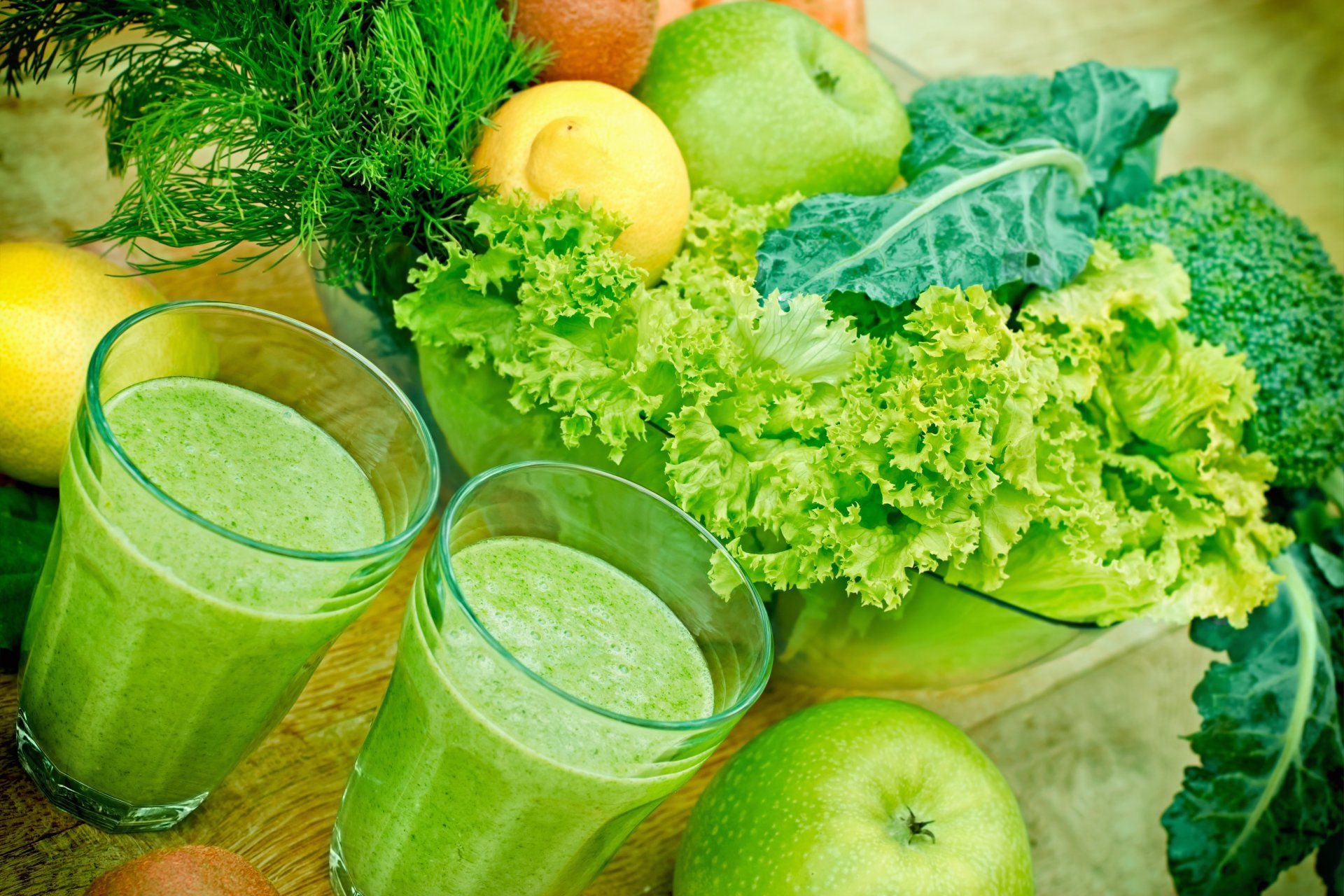 Zwei Gläser grüner Saft, umgeben von Obst und Gemüse