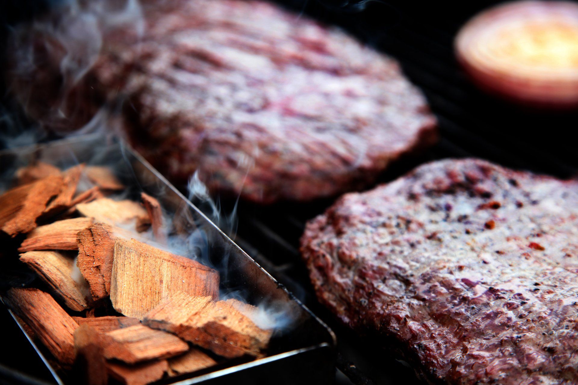 Closeup of a smoking tray of Western Smoking chips and flank steaks on a grill