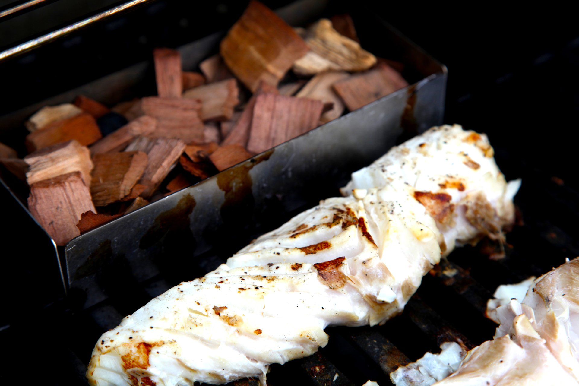 Closeup of Mahi Mahi cooking on the grill with a tray of smoking chips next to it