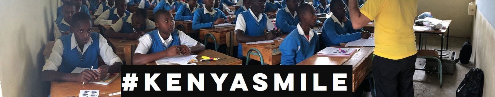A group of people are sitting at tables in front of a sign that says kenya smile.