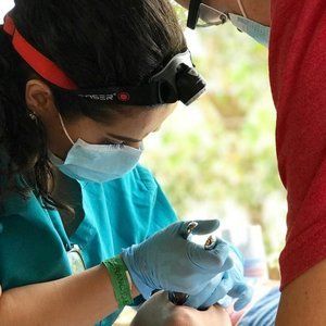 A woman wearing a mask and gloves is working on a child 's teeth.