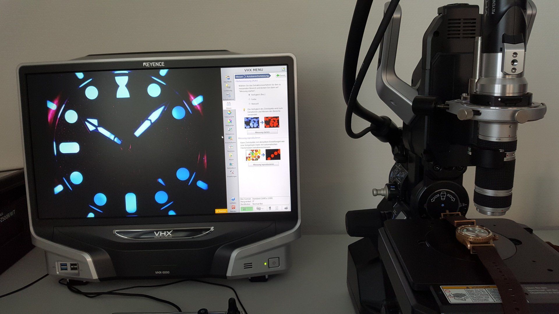 A microscope is sitting on a table next to a computer monitor.