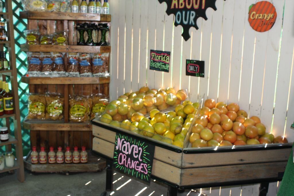 Oranges for sale at an outdoor market stall, wooden display case, other packaged goods on shelves.