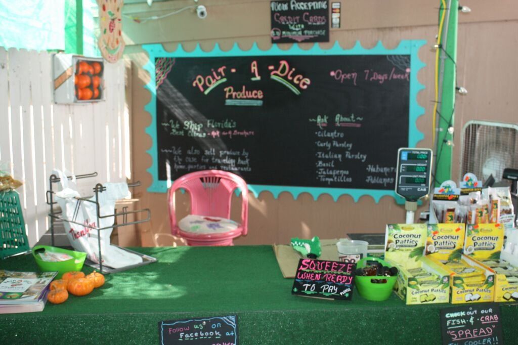 Produce stand with chalkboard menu, pink chair, and various fruits and vegetables for sale.
