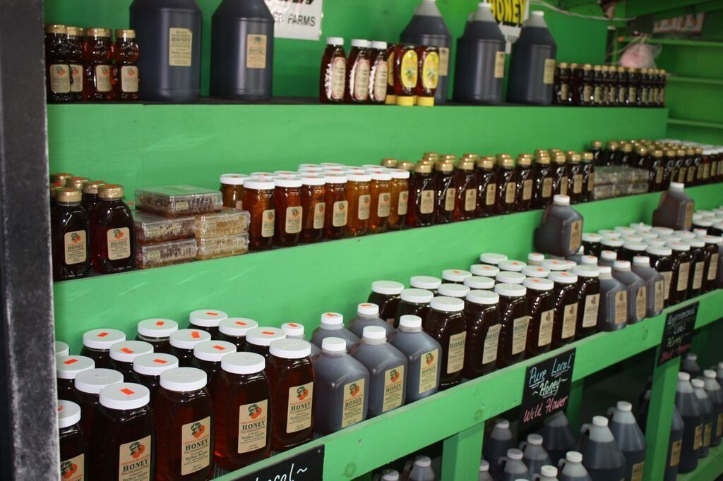 Shelves filled with various honey jars and bottles in shades of brown, with green shelving in a store.