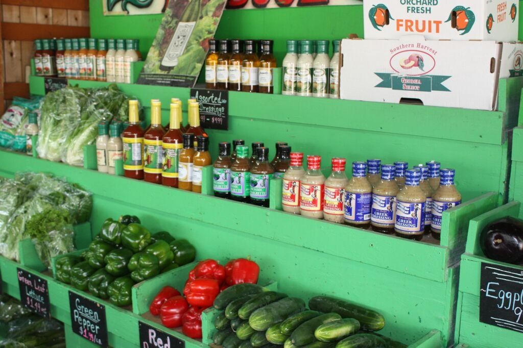 Green farm stand display of produce, sauces, and condiments.