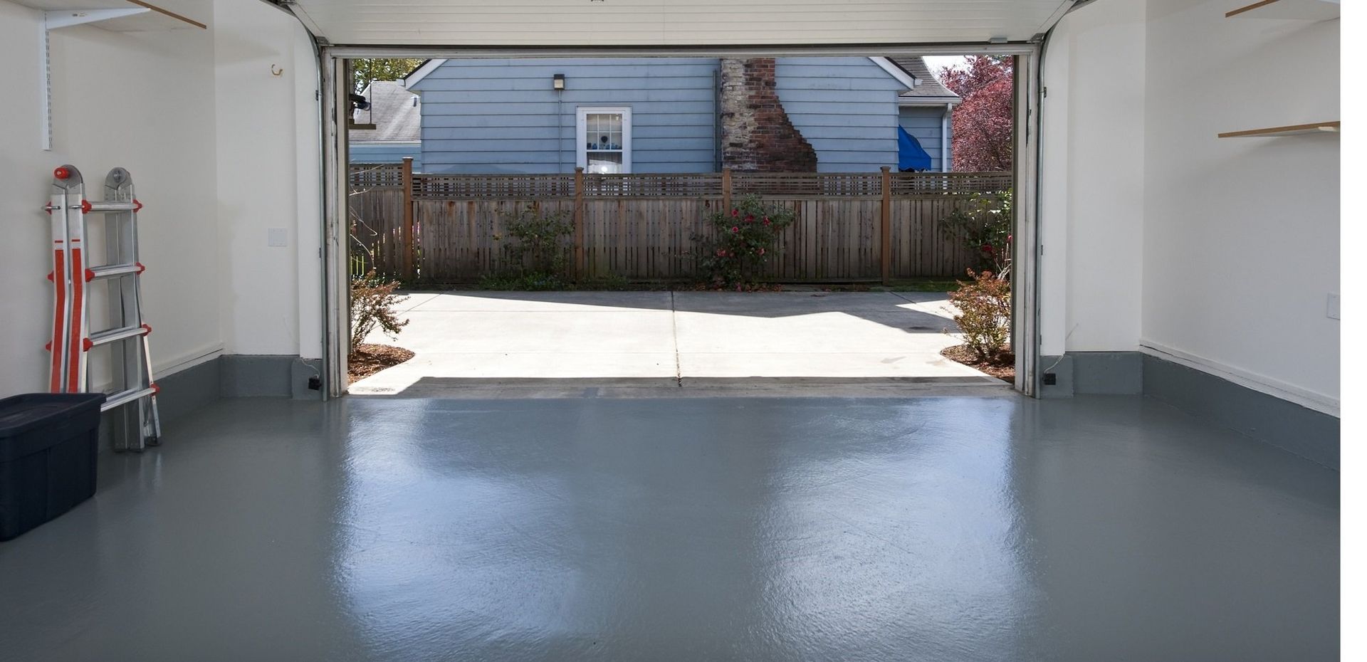 a garage with the door open and a blue house in the background .