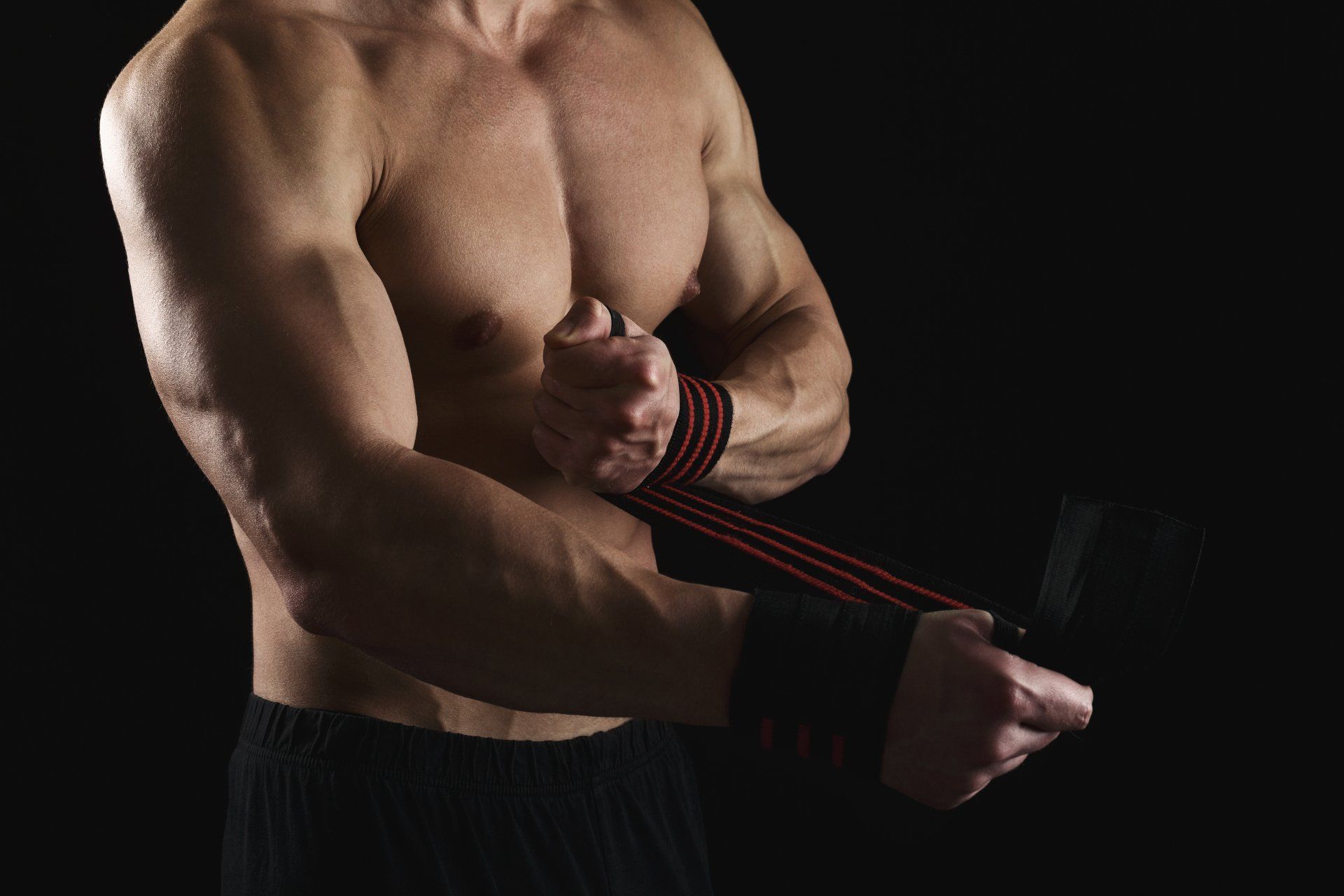 A shirtless man is wrapping his wrist with a wristband.