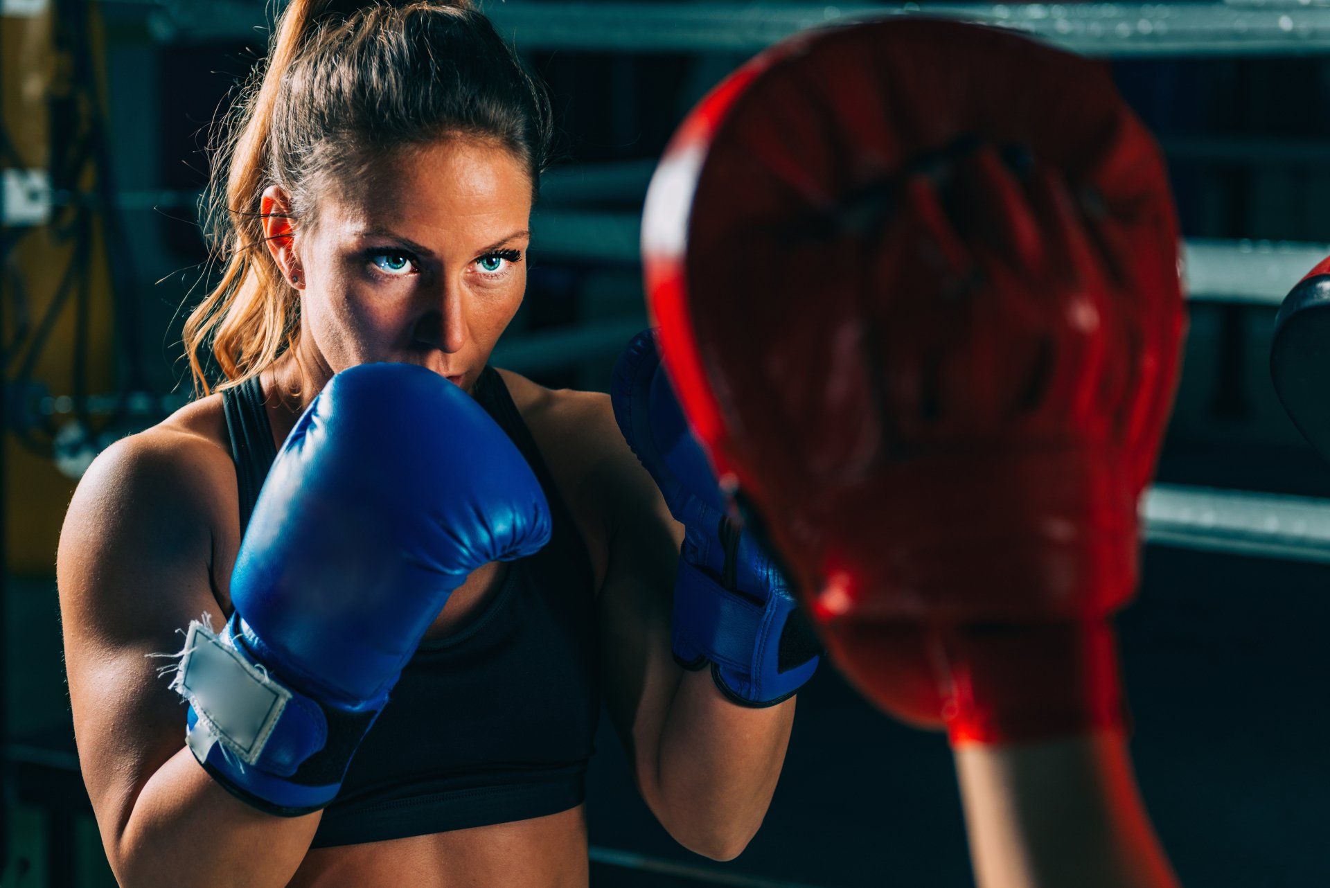 A woman is wearing blue boxing gloves in a boxing ring.