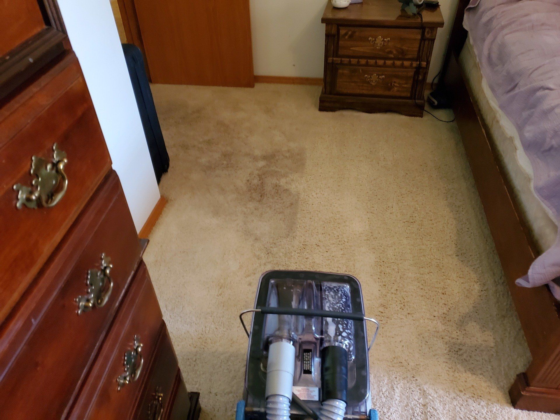 A vacuum cleaner is sitting on the floor in a bedroom next to a bed.