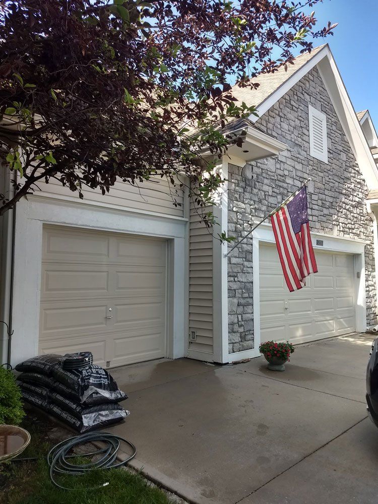 Suburban house exterior with two-car garage, American flag, and stacked soil bags by the driveway