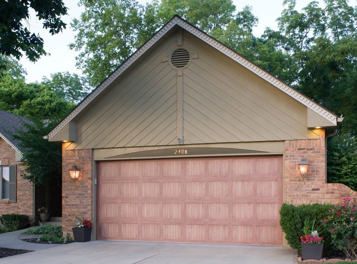 Suburban home garage with tan siding, pink double door, and lit wall lanterns at dusk