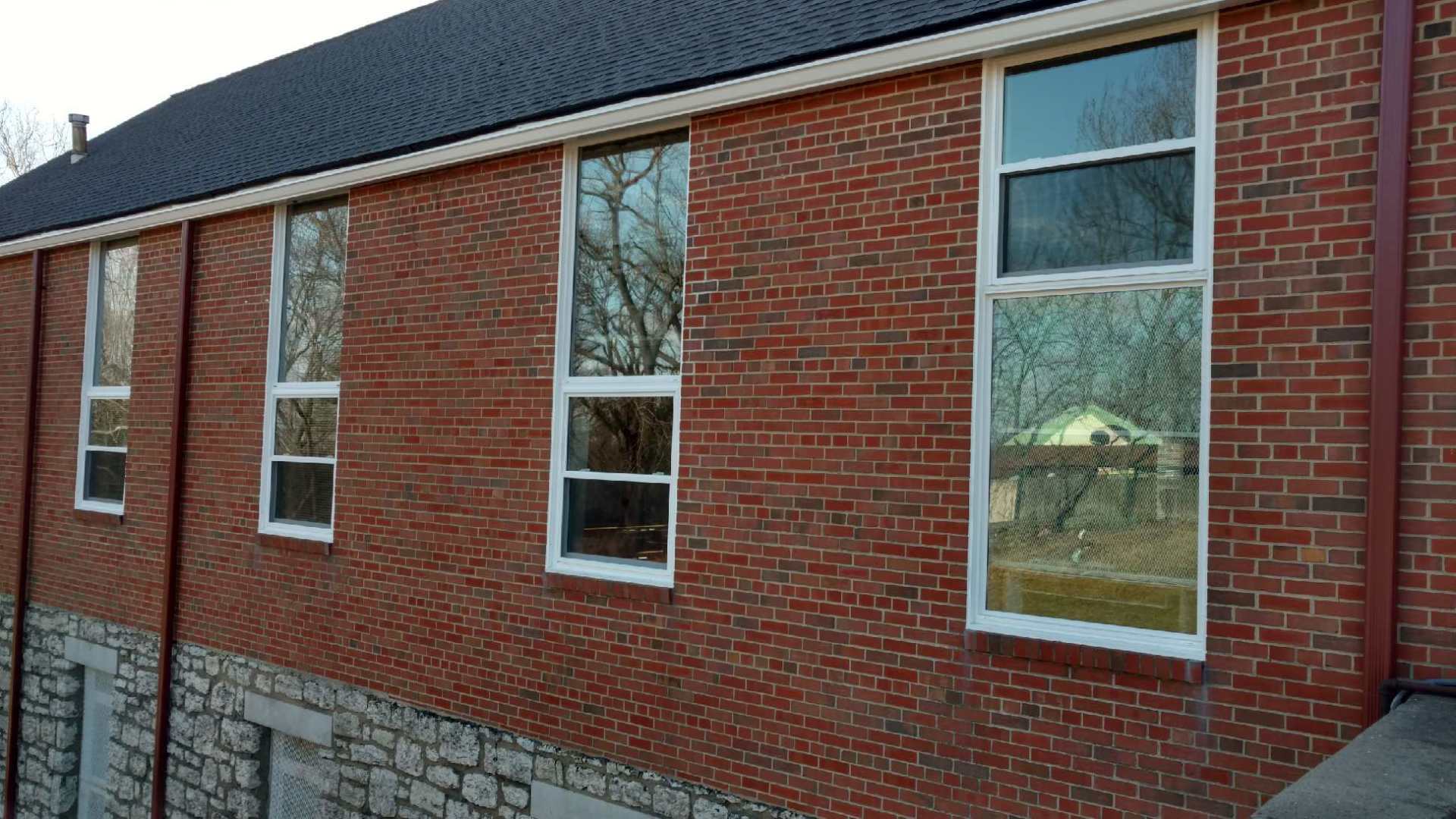 Red brick building exterior with several tall windows and a stone foundation under a dark roof.