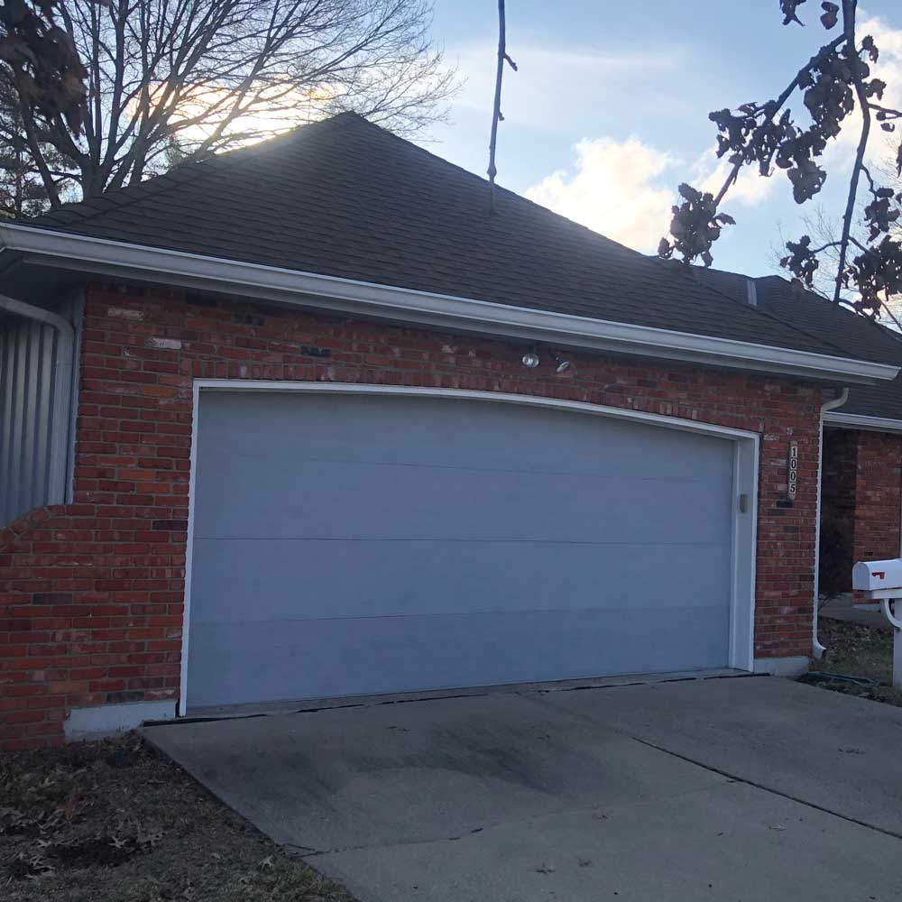 Brick house with a closed light gray garage door and concrete driveway at sunset