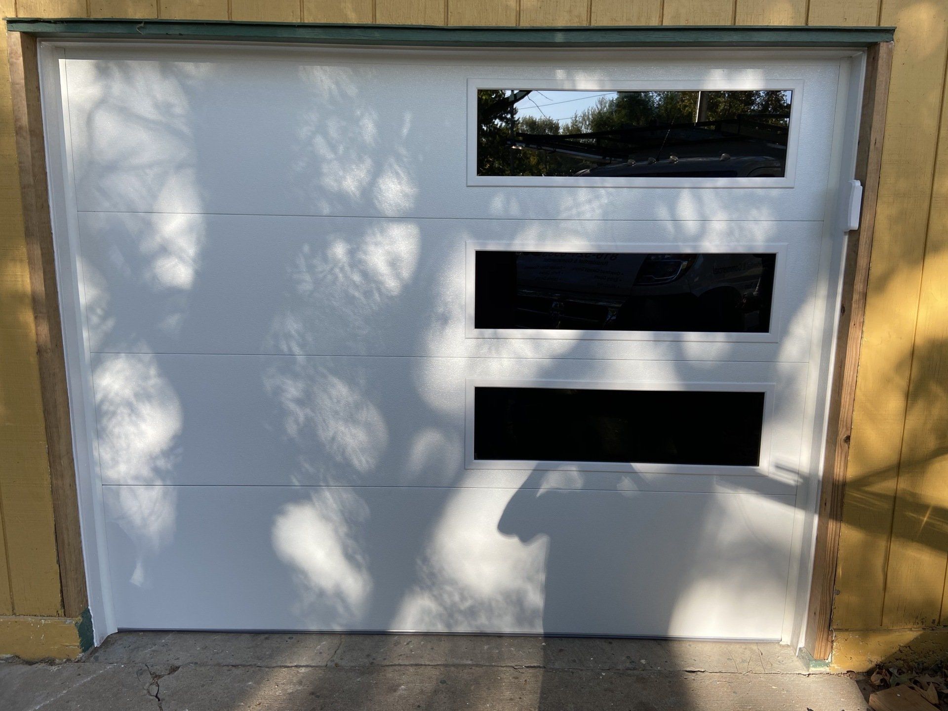 White garage door with three narrow windows, partly shaded by tree shadows.