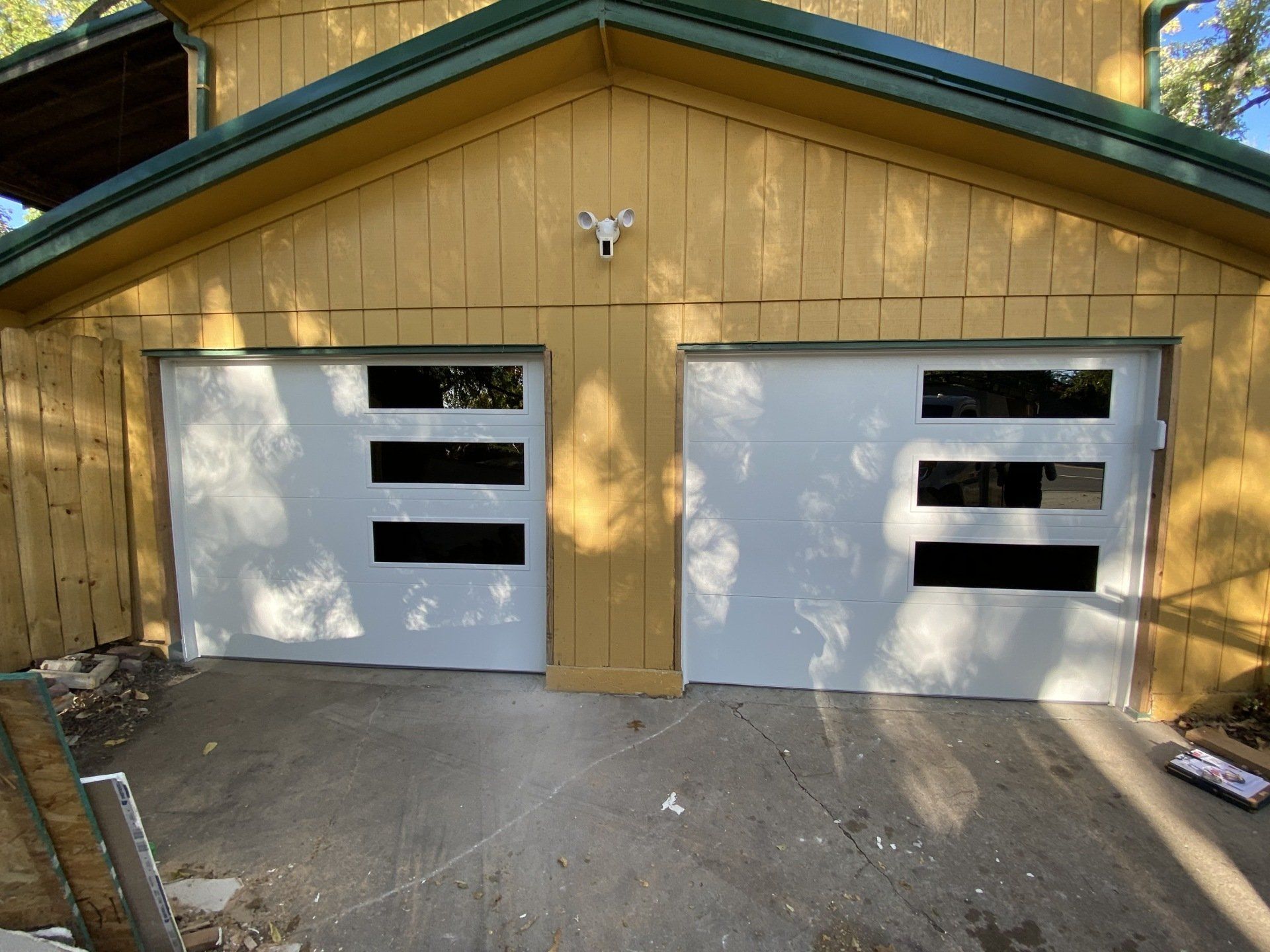 Two white garage doors on a tan detached garage with a green roof trim, viewed from the driveway