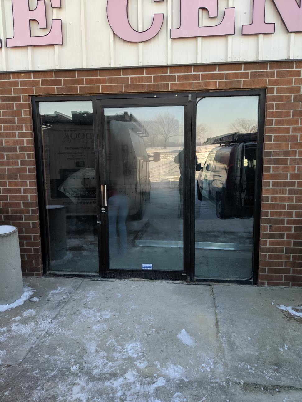 Glass double doors on a brick storefront with snow on the sidewalk.
