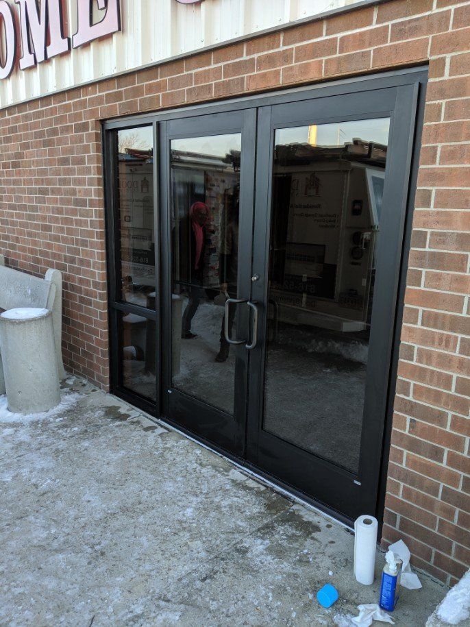 Black double glass doors in a brick building entrance with snow on the ground.