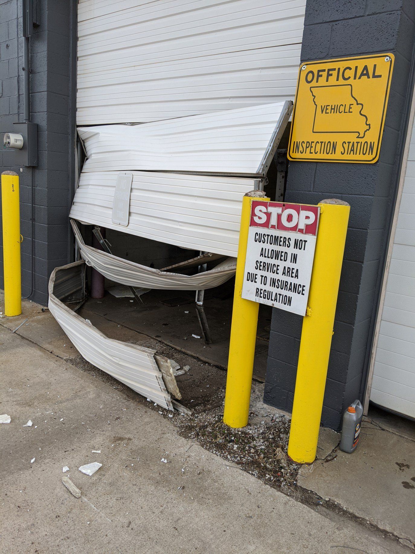 Damaged white roll-up door smashed inward beside yellow bollards and warning signs at a loading dock