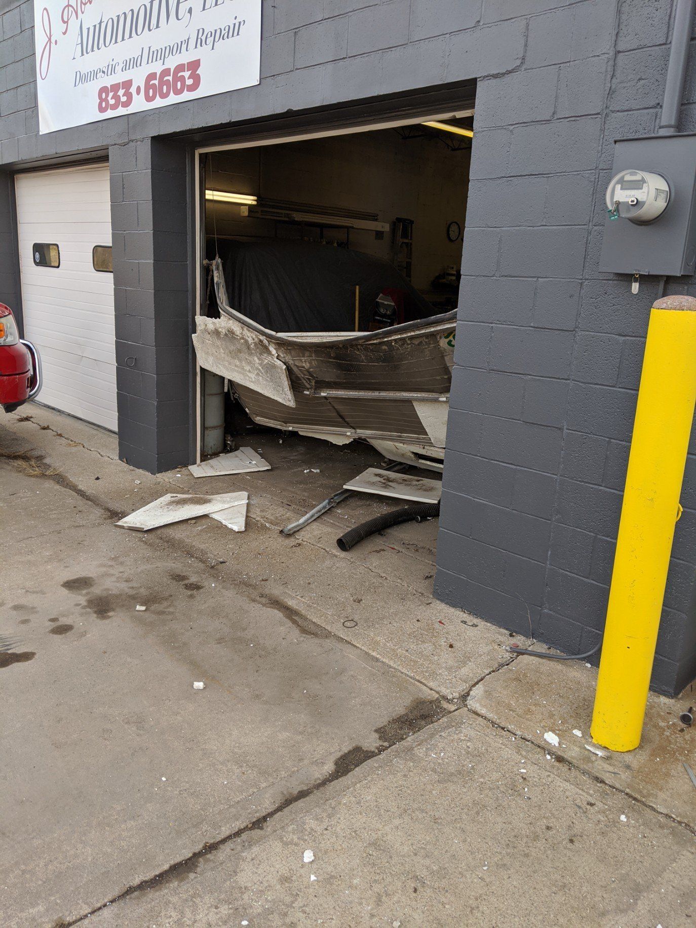 Car crashed through a garage door, leaving the metal entrance bent and debris on the sidewalk.