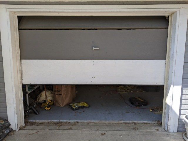 Partially open white garage door with clutter inside a dim storage space