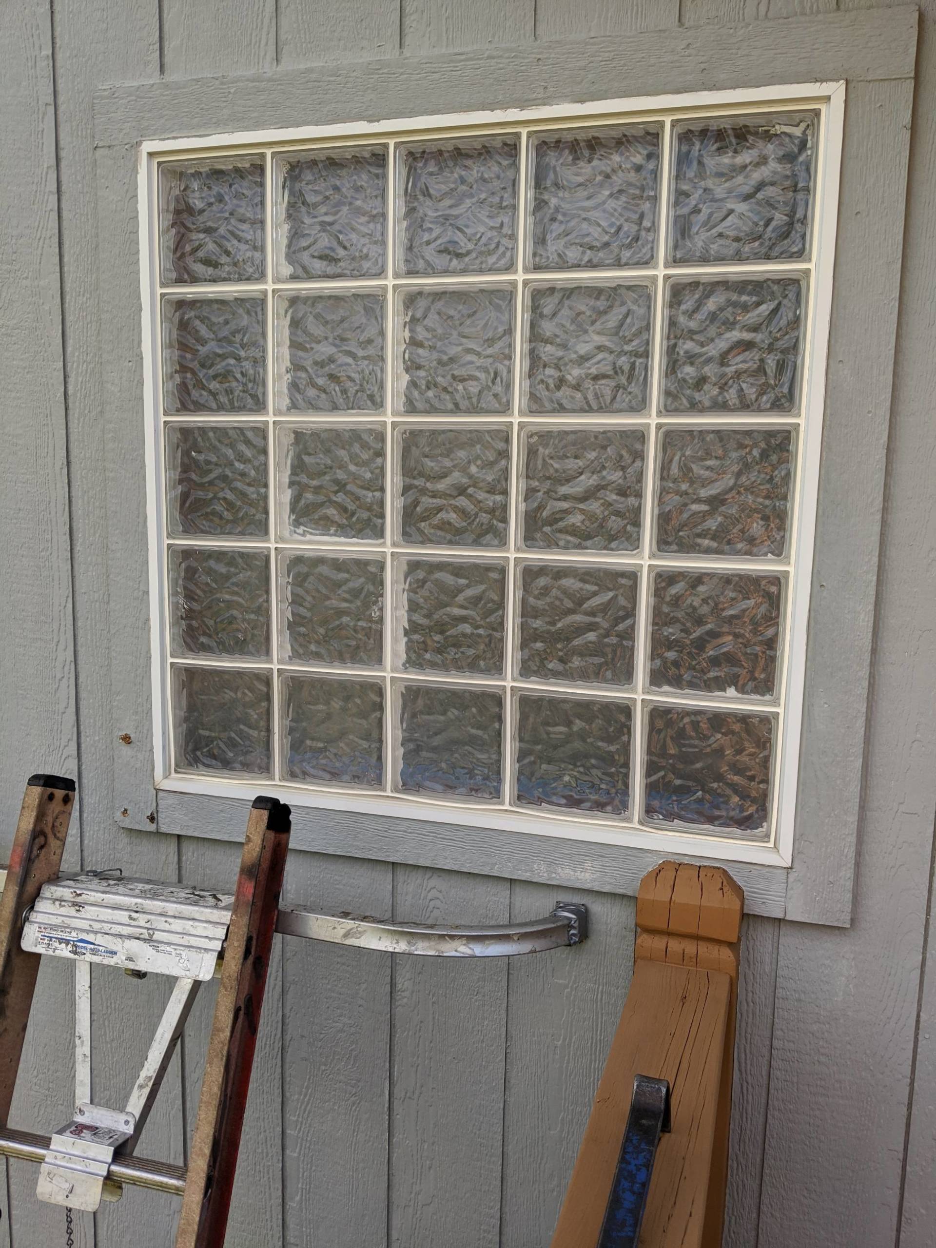 White-paned window on a gray wall with a folded step ladder and tools leaning below it