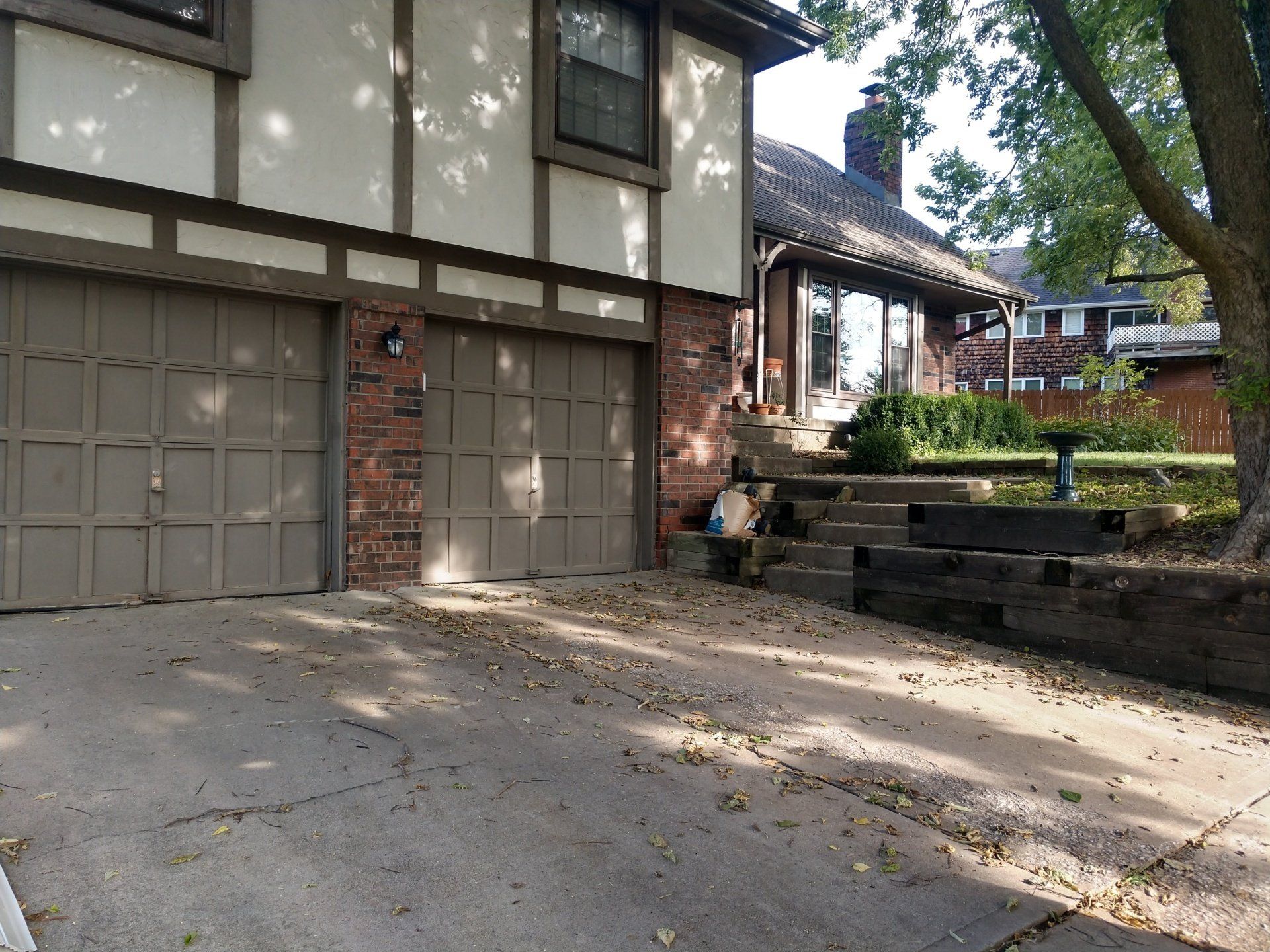 Front of a Tudor-style house with garage, driveway, and stone steps leading to a landscaped yard