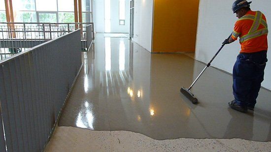 Worker in orange vest polishing a glossy floor in a bright indoor hallway