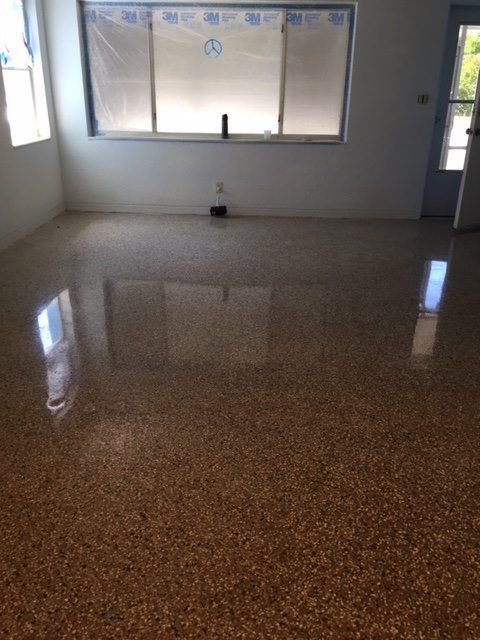 Empty room with polished speckled floor, large window, and door on the right.