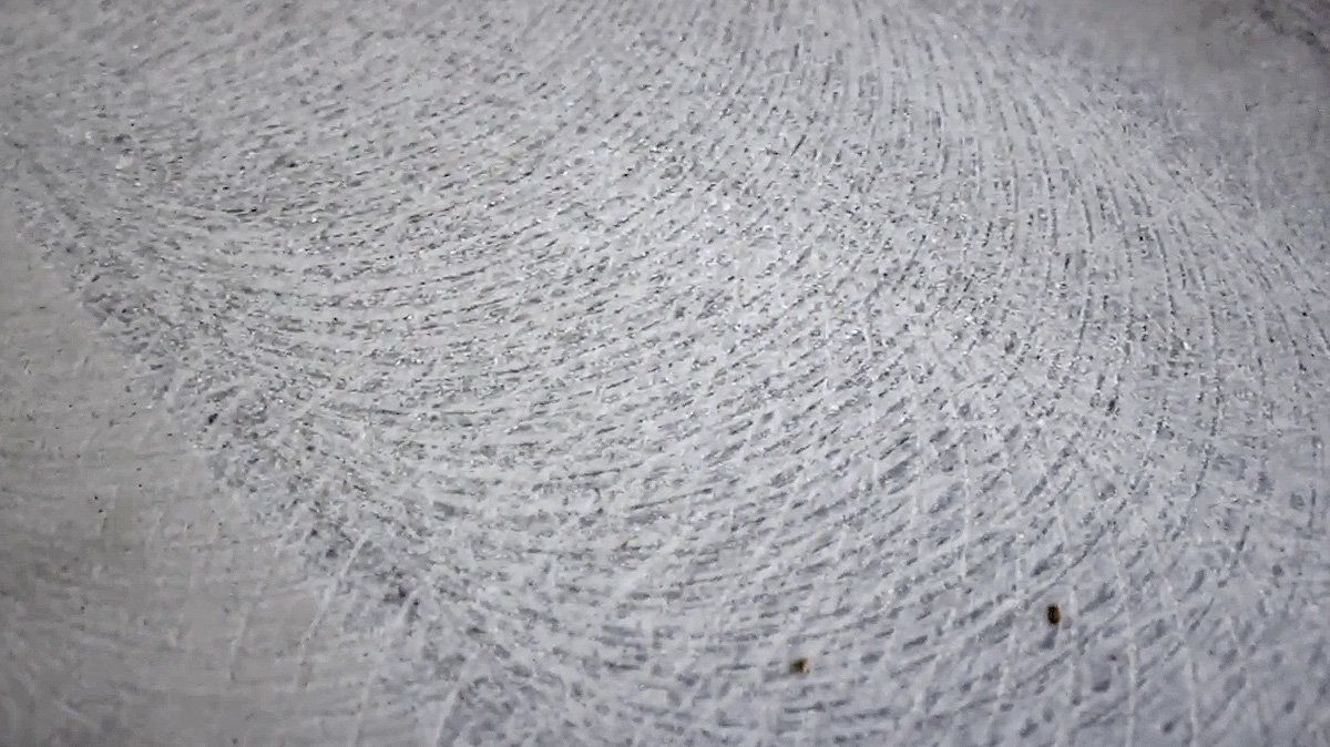 Close-up of a light gray textured surface with scattered specks and curved brush-like marks