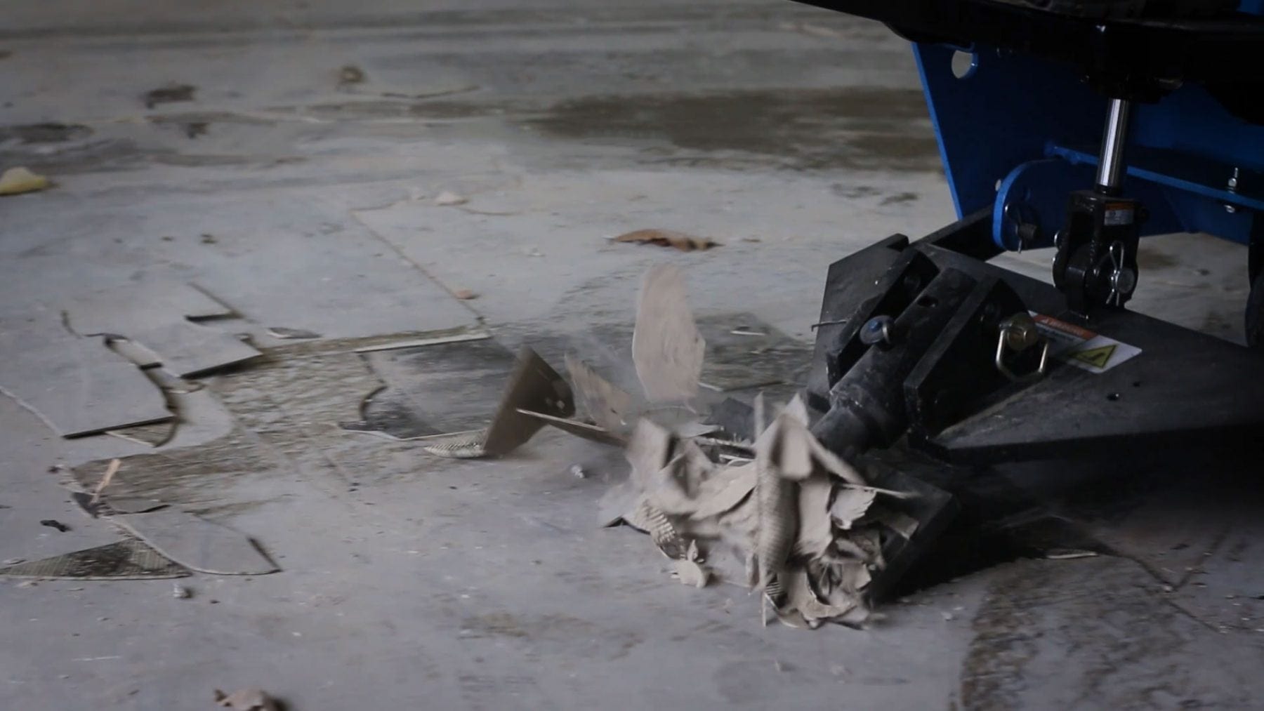 Black industrial machine grinding concrete, sending dust and debris across a gray floor.