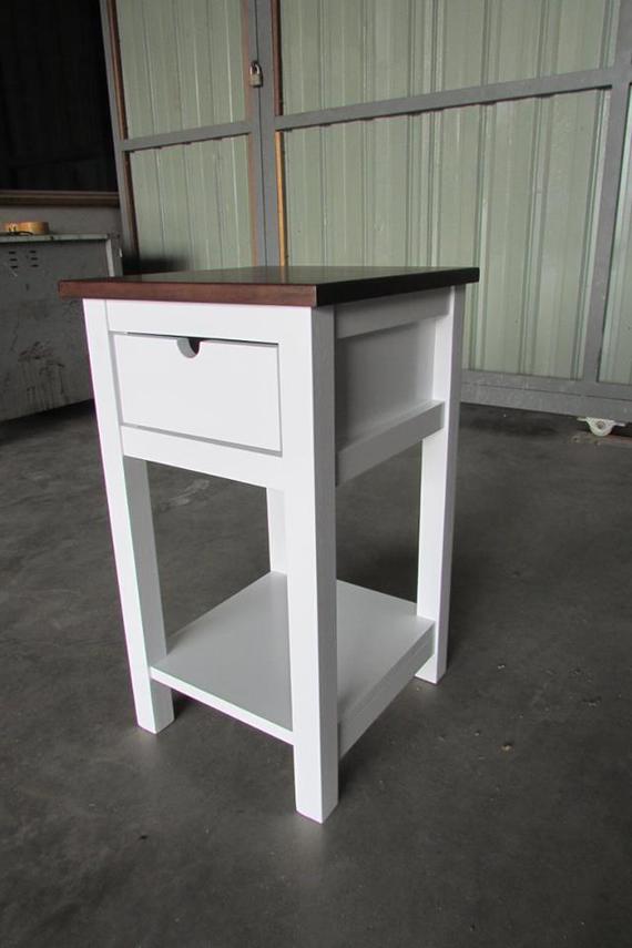 White nightstand with brown top, a drawer, and shelf on a concrete floor.