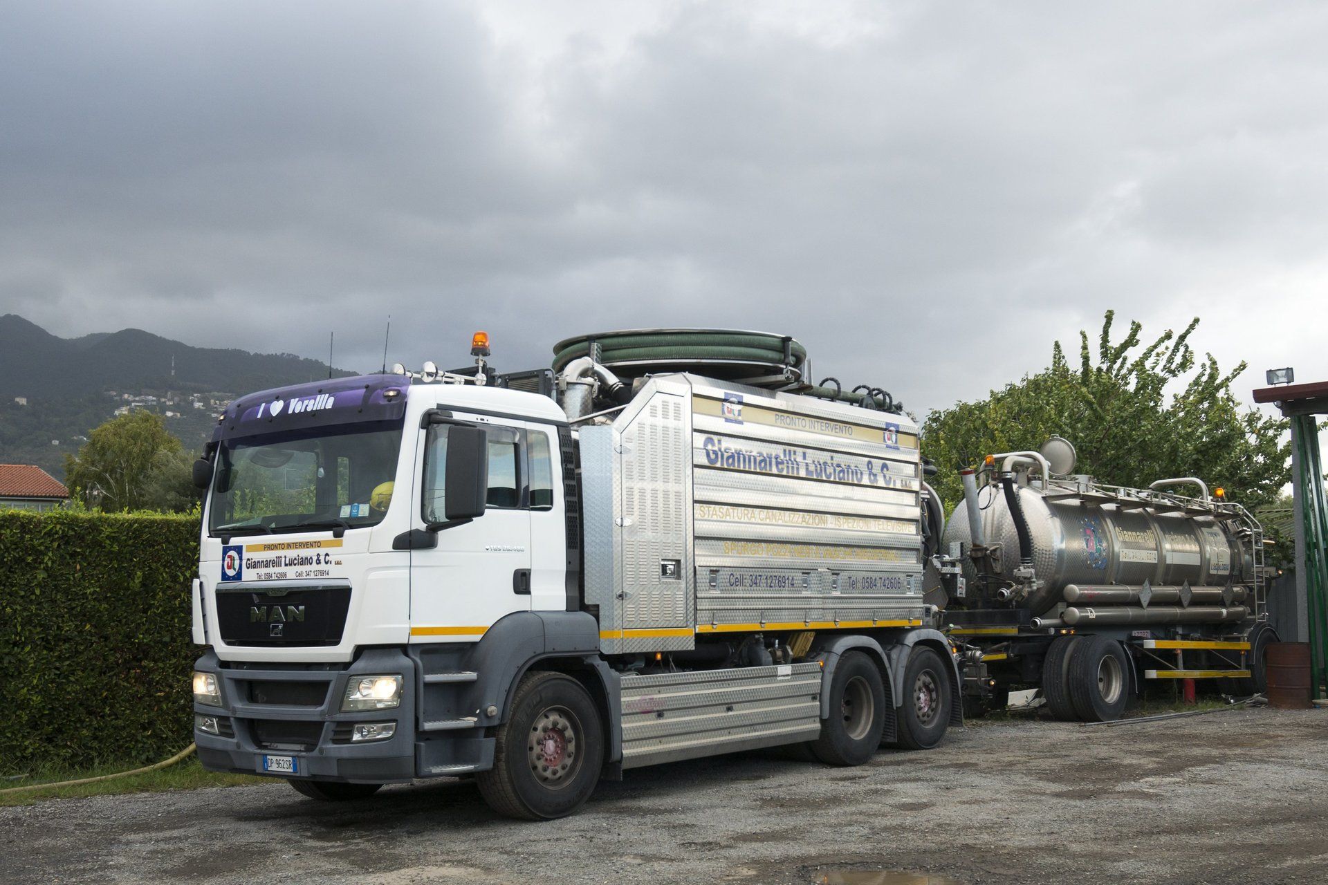Camion bianco e rimorchio con serbatoio argentato, parcheggiati fuori.