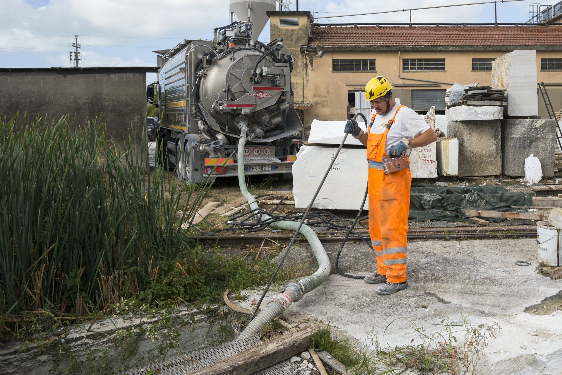 Un uomo in tuta arancione guida un autospurgo vicino all'acqua e a un edificio.