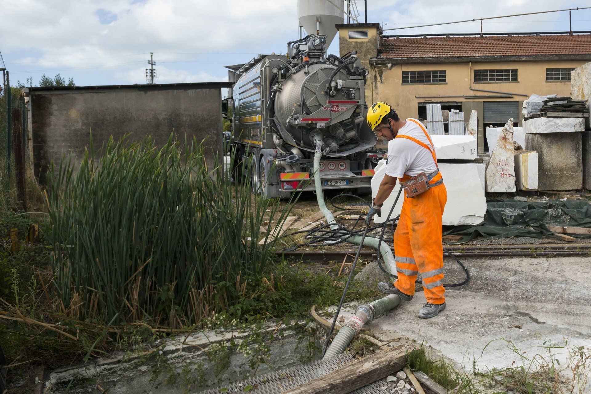 Un uomo in tuta arancione guida un autospurgo vicino all'acqua e a un edificio.