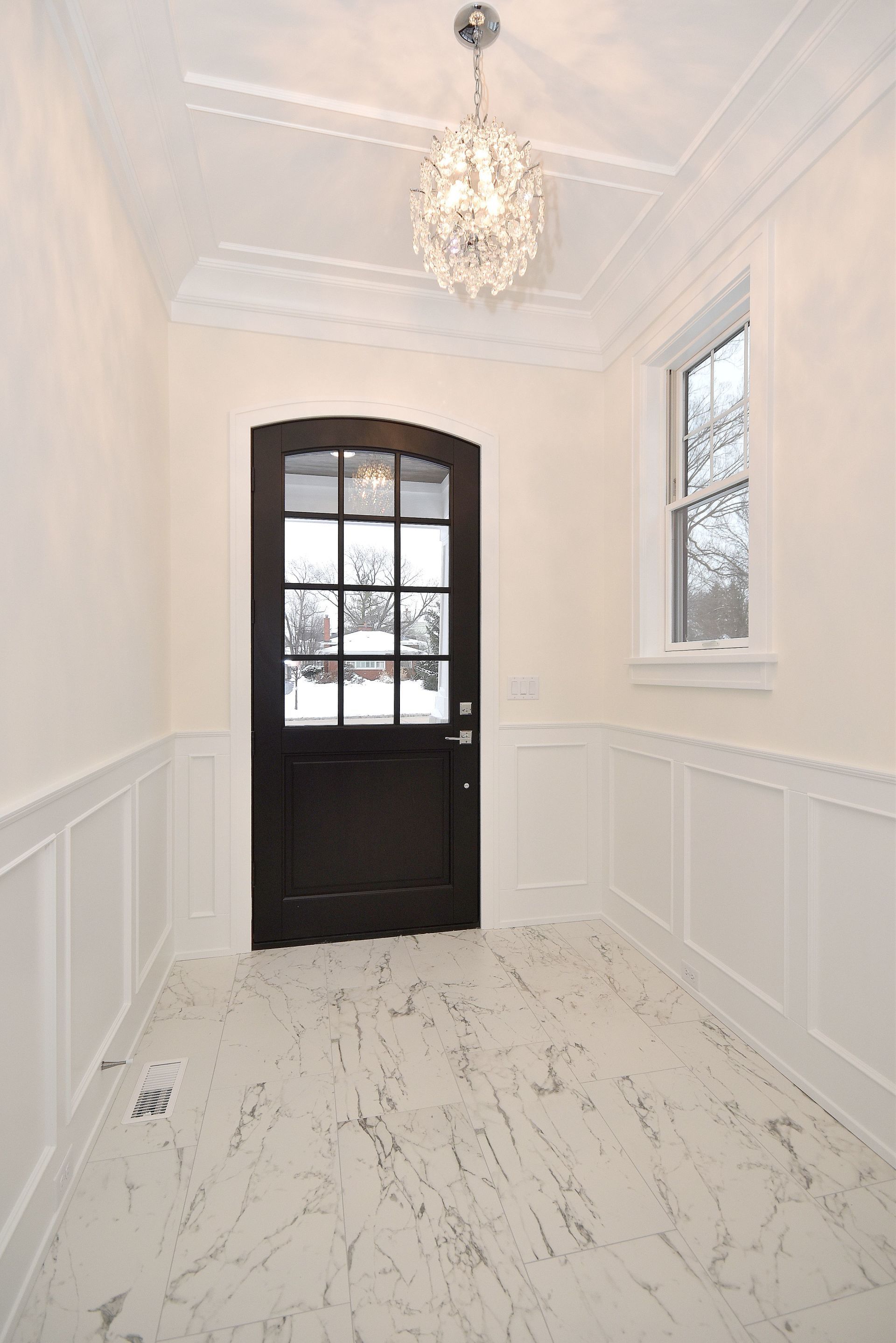 A hallway with a black door and a chandelier hanging from the ceiling.