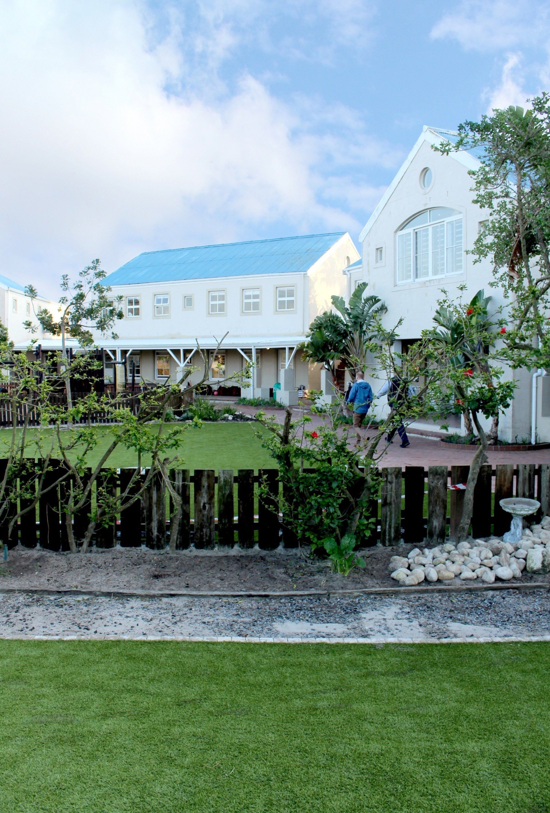 a large white building with a blue roof is surrounded by a lush green yard .