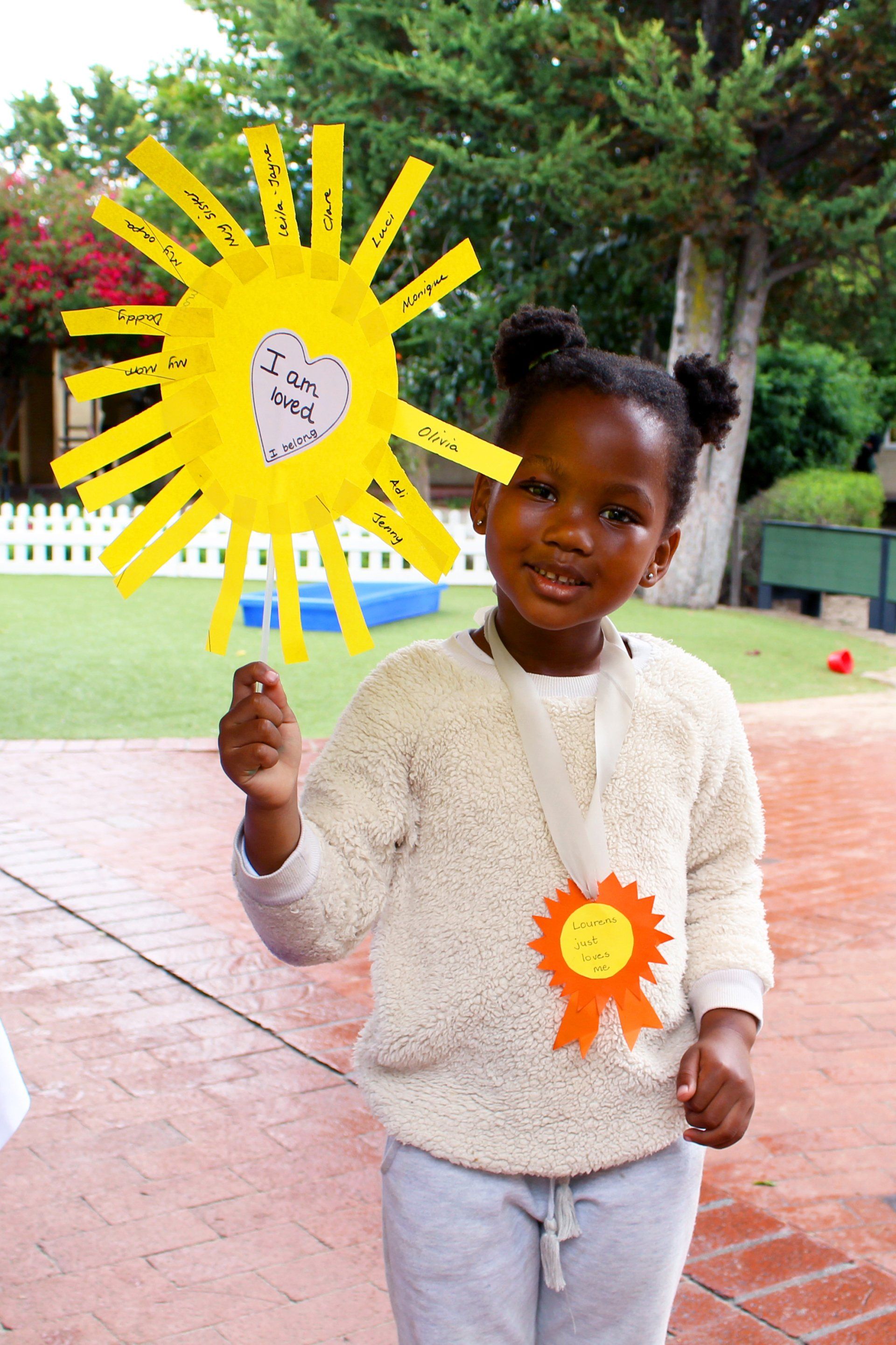 a little girl is holding a paper sun with a heart on it