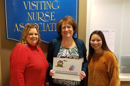 Three women are standing next to each other in front of a sign that says visiting nurse association