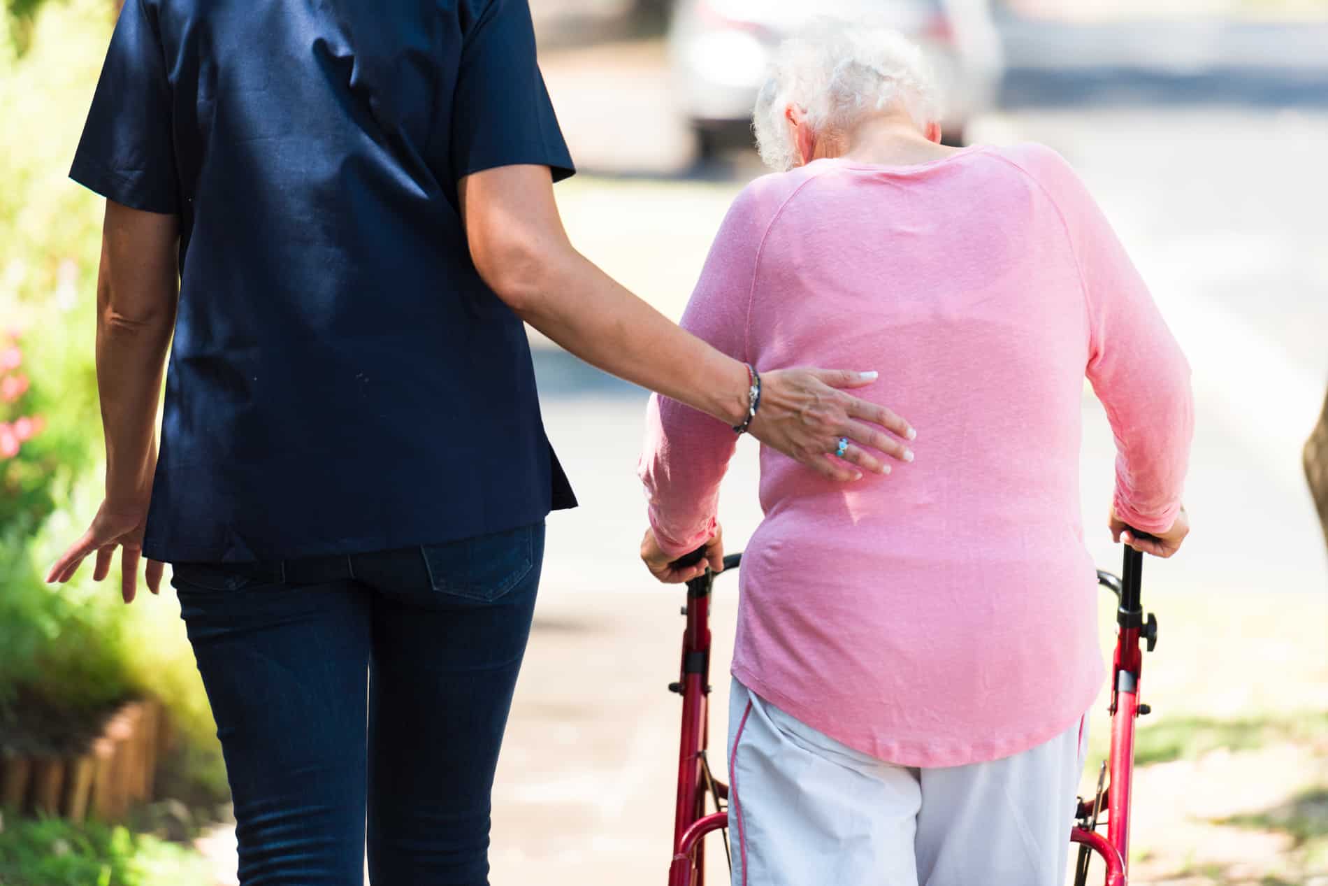 A woman is helping an elderly woman with a walker.