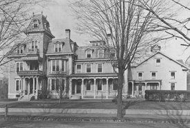 A black and white photo of a large house surrounded by trees.