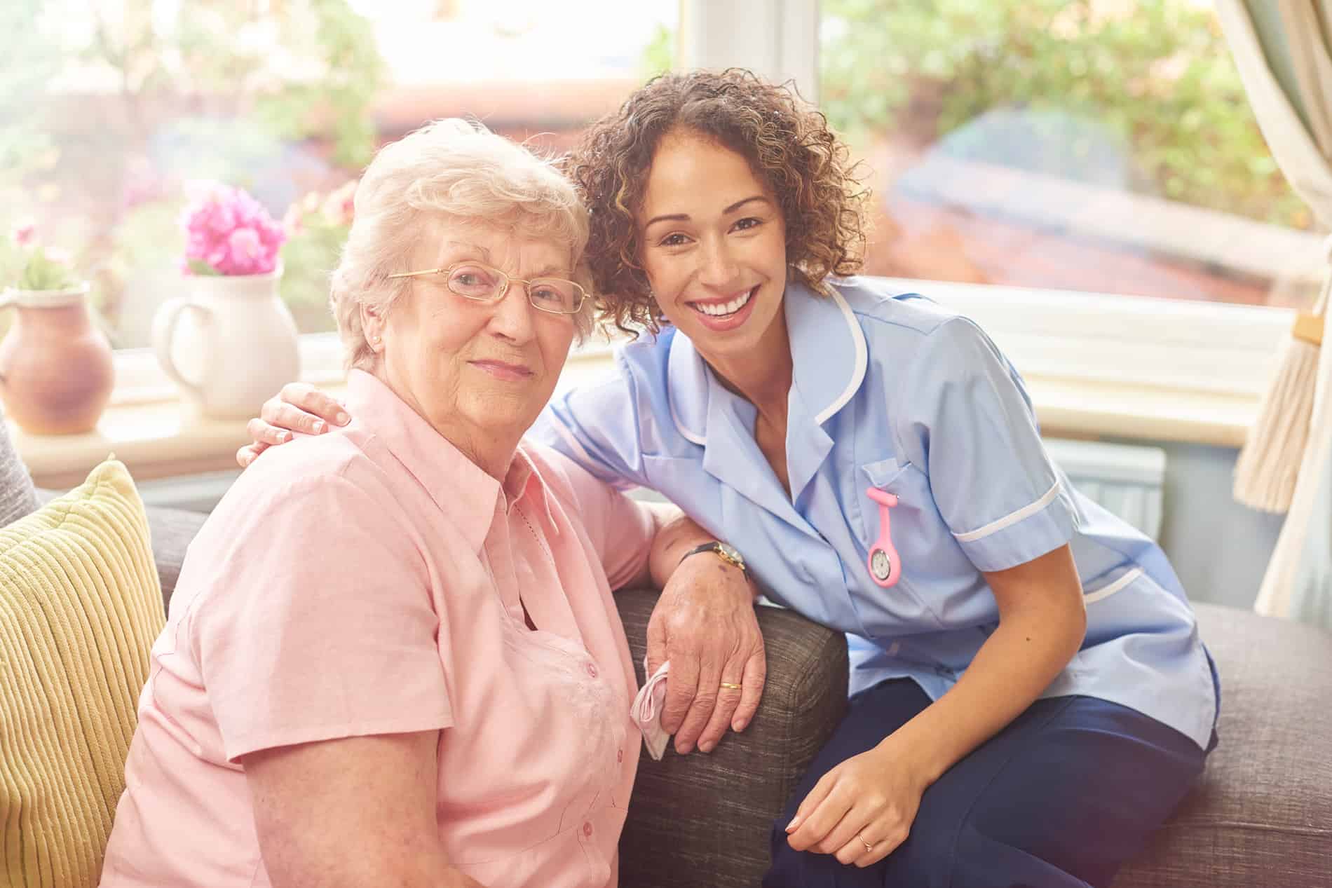 A nurse is sitting next to an older woman on a couch.